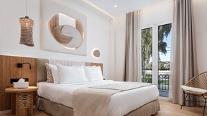 A modern bedroom with a large bed, a bedside table with a tissue box, a wall-mounted light fixture, and a view of the outdoors through a sliding door. - Aegina Dream Suites (Aegina)