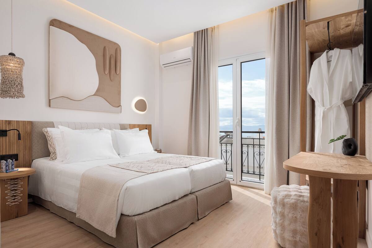 Une chambre moderne avec un grand lit, une table de chevet, un luminaire suspendu et une vue sur l’extérieur grâce à une porte-fenêtre coulissante.