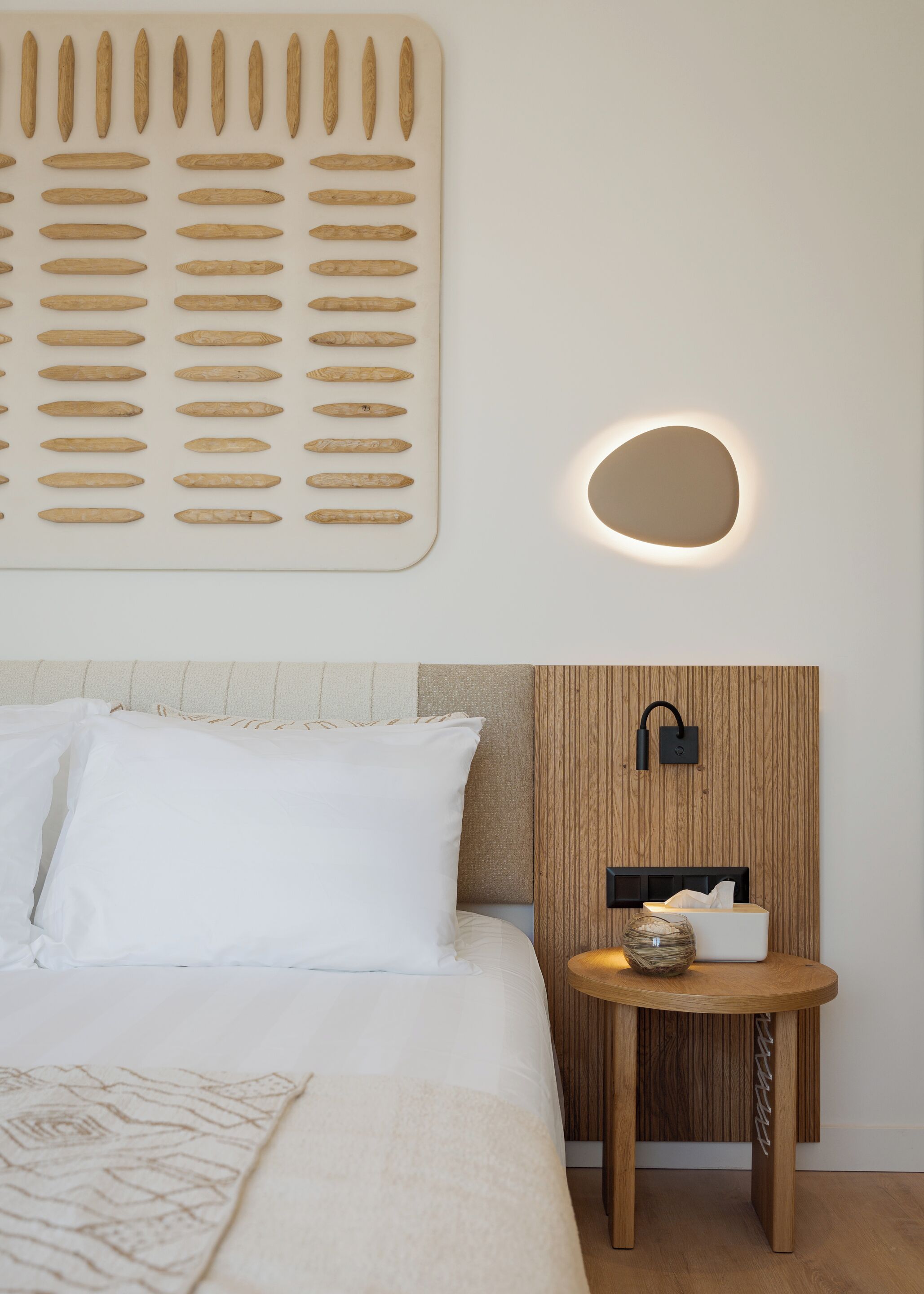 A neatly arranged hotel room with a bed, pillows, a bedside table with a lamp, and a wall-mounted mirror.