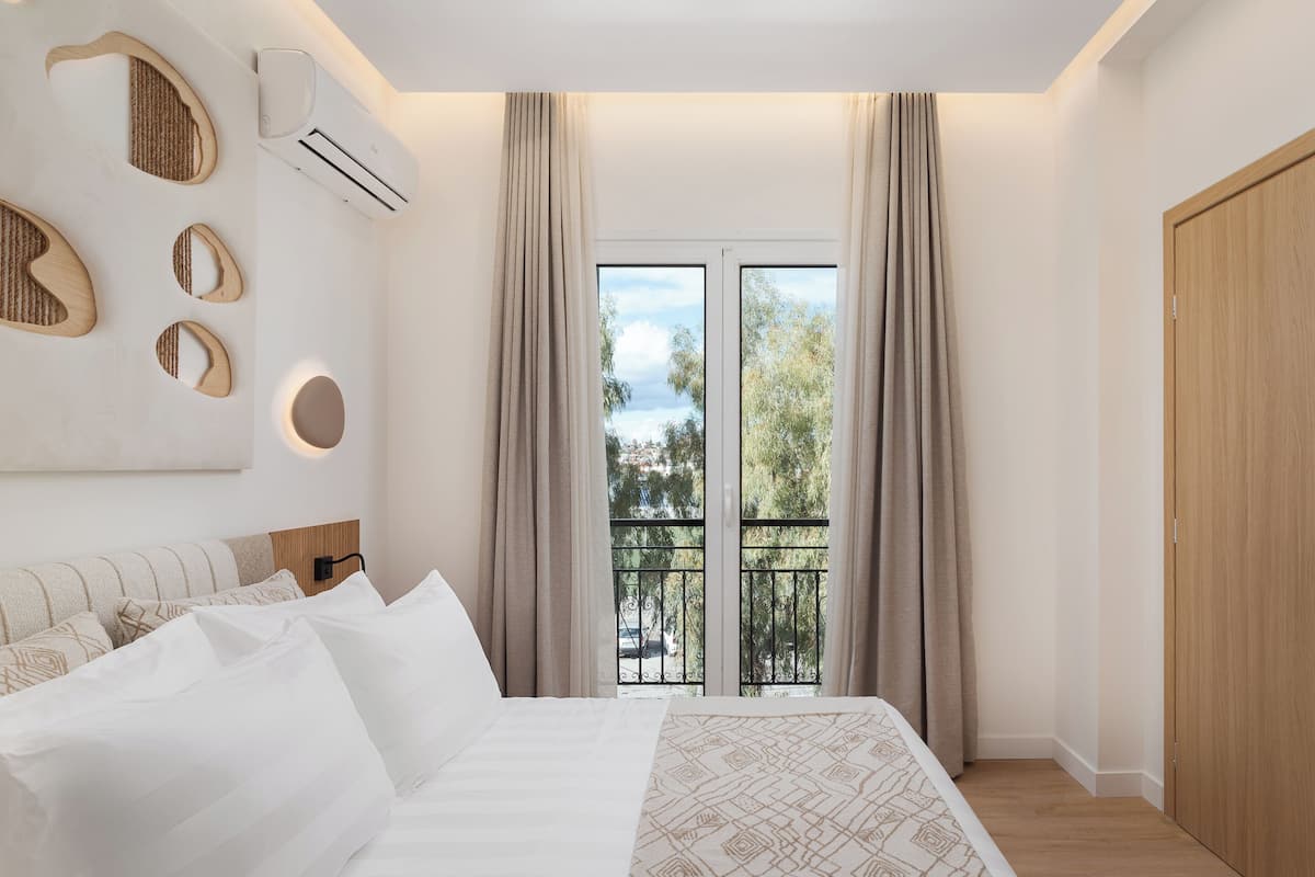 Une chambre à coucher avec un lit, une fenêtre avec des rideaux, un appareil de climatisation et une porte en bois.