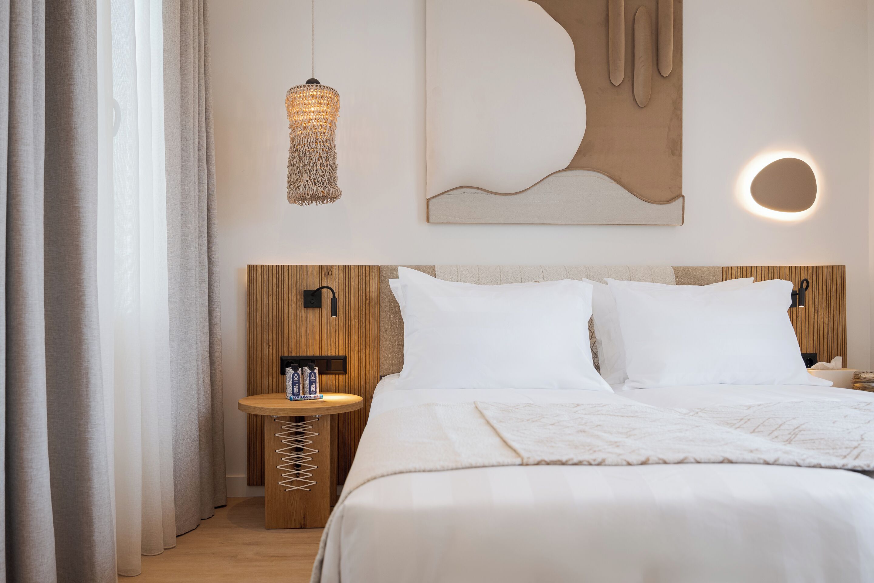 A neatly arranged hotel room with a bed, bedside table, lamp, and abstract wall art.