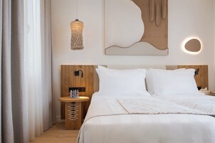 Habitación de hotel ordenada con cama, mesita de noche, lámpara y arte abstracto en la pared.