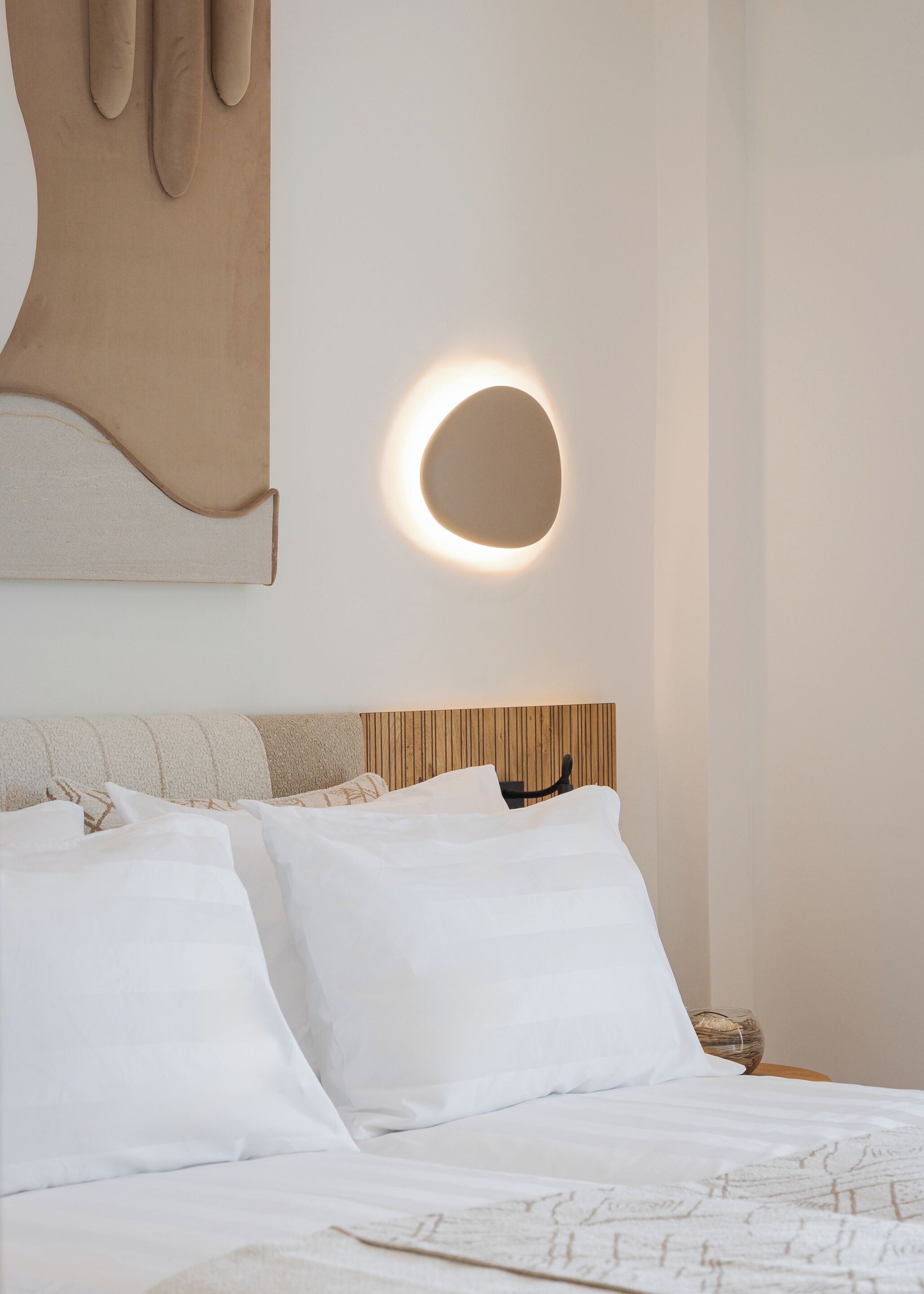Camera da letto moderna con una testiera in legno, una lampada a parete rotonda e un'ampia opera d'arte astratta.
