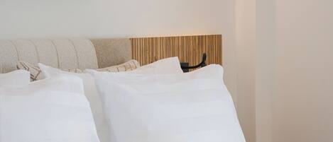 A modern bedroom with a wooden headboard, a round wall light, and a large abstract artwork.