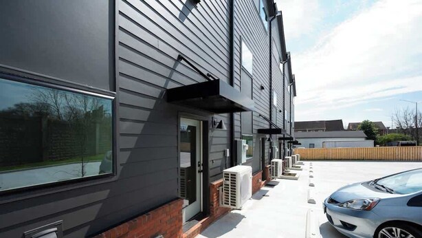 A modern building with a grey exterior, a brick foundation, and a row of air conditioning units along the side.