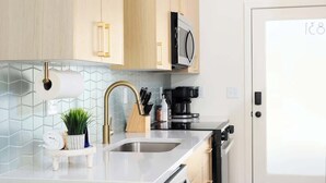 A modern kitchen with light wood cabinets, a stainless steel sink, and a microwave.