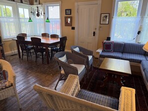 A cozy living room with a dining table, wicker chairs, a sofa, and a patterned rug.