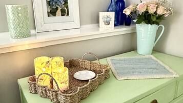 A green dresser with drawers, a woven basket with candles, a framed picture, and decorative vases.