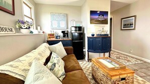 A cozy living room with a brown couch, a coffee table, and a kitchen area with a refrigerator and cabinets.