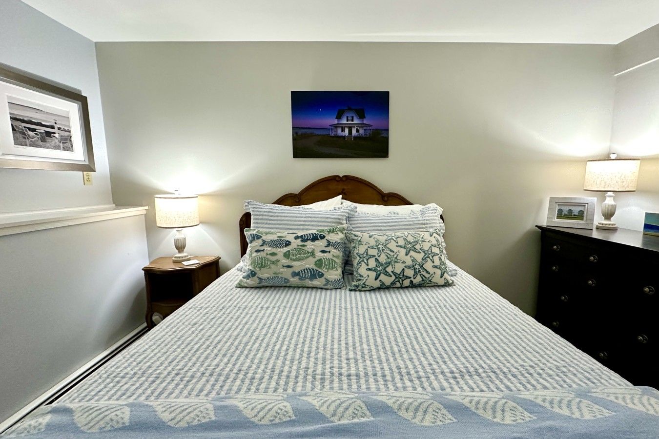Ein Schlafzimmer mit einem Bett, zwei Nachttischen, einer Kommode und einem gerahmten Bild an der Wand.