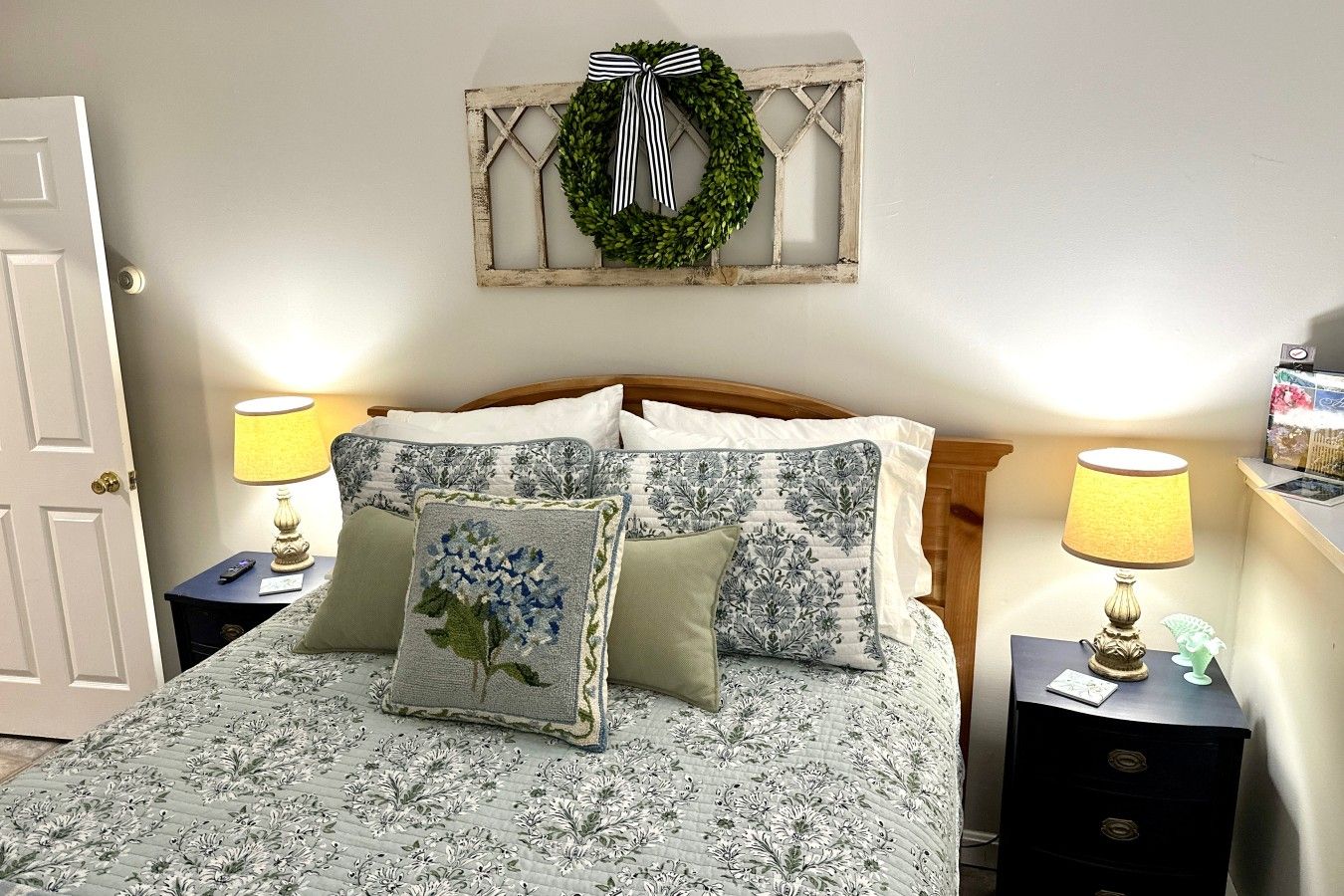 A bedroom with a bed, two nightstands, a wall-mounted light fixture, and a decorative wreath.
