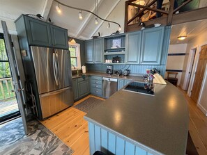A kitchen with blue cabinets, stainless steel appliances, and a wooden deck outside.