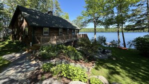 Una baita di legno con veranda, circondata da alberi e un lago.