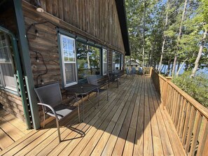 En träveranda med utomhusmöbler och fönster med utsikt över en vattenyta.