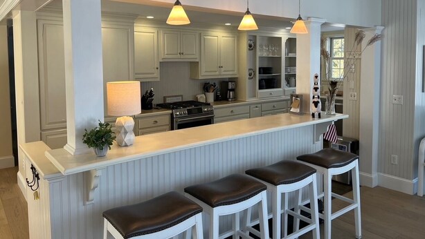 A kitchen with a central island, bar stools, pendant lighting, and a view into the dining area. - GOLDEN OWL - Town of Owls Head (Owls Head)
