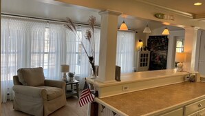 A spacious living room with a beige sofa, a small side table with a lamp, and a large window with sheer curtains. - GOLDEN OWL - Town of Owls Head (Owls Head)