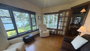 Uma sala de estar espaçosa com grandes janelas, um canto de estar acolhedor e vista para um lago.
