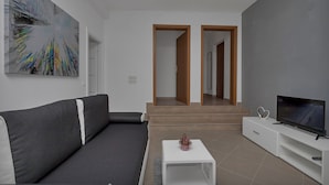 Ein modernes Wohnzimmer mit einem grauen Sofa, einem weißen Couchtisch, einem Flachbildfernseher und einem großen abstrakten Gemälde an der Wand.