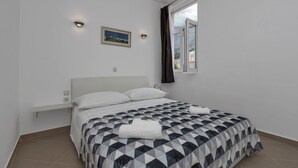 Ein Schlafzimmer mit Bett, Nachttisch, Wandleuchte, Fenster mit Vorhängen und einem Bild an der Wand.