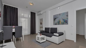 Ein modernes Wohnzimmer mit einem weißen Sofa, einem kleinen weißen Couchtisch und einem Essbereich mit Tisch und Stühlen – alles in Weiß.