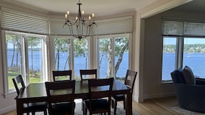 A dining area with a table and chairs, large windows with a view of a lake, and a chandelier. - BELFAST ON THE BAY - Town of Belfast (Belfast)