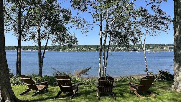 A lakeside seating area with wooden chairs and a picnic table, surrounded by trees and a view of the water. - BELFAST ON THE BAY - Town of Belfast (Belfast)