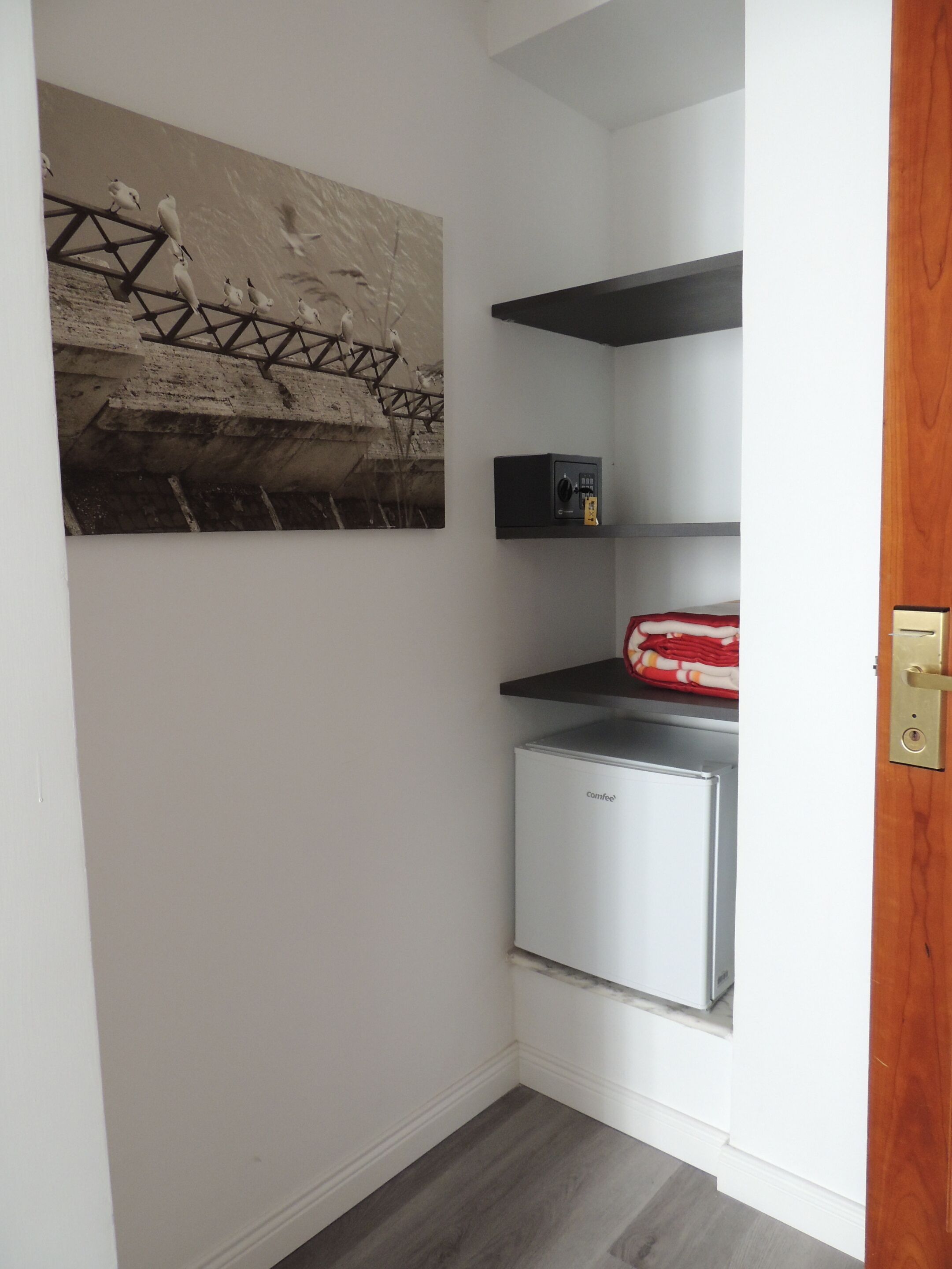 A compact kitchen with a built-in refrigerator, a coffee machine, and a shelf with a red and white patterned cloth.