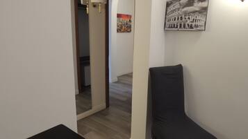 Un corridoio stretto con una sedia nera, un muro bianco con un quadro che raffigura il Colosseo e una porta che dà su un'altra stanza.