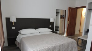 A neatly made bed with a patterned bedspread, a dark headboard, and two wall-mounted lamps. - Madonna della Neve (Rome)