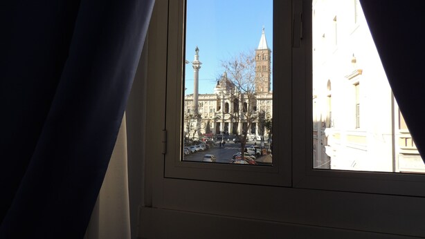 A window with a view of a historic building with a tower and a statue in the foreground. - Madonna della Neve (Rome)
