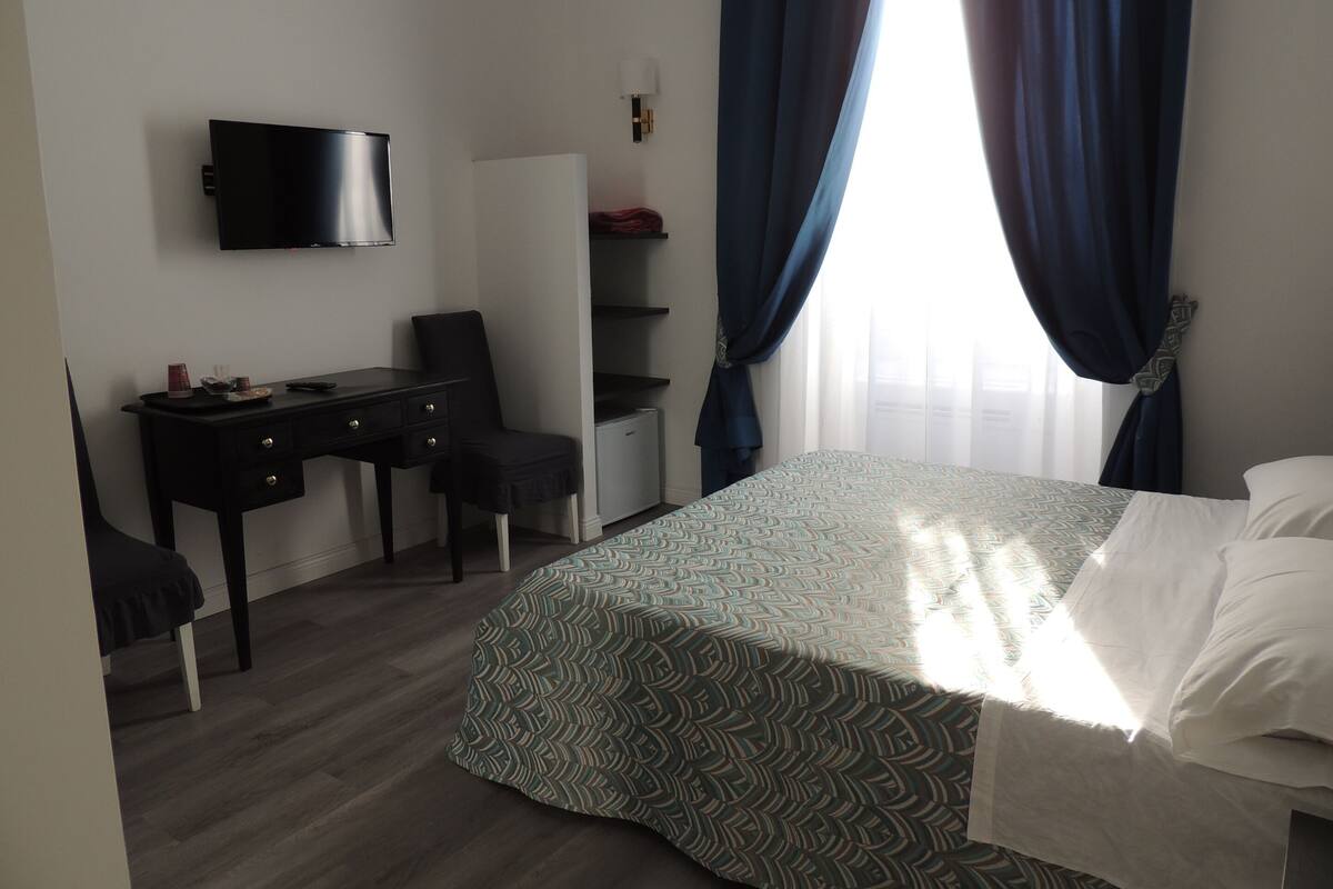 A hotel room with a bed, a desk, a chair, a TV, and a wardrobe.