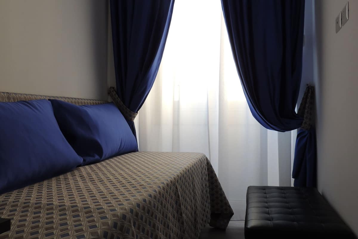 A room with a bed, a bench, and a window with curtains.