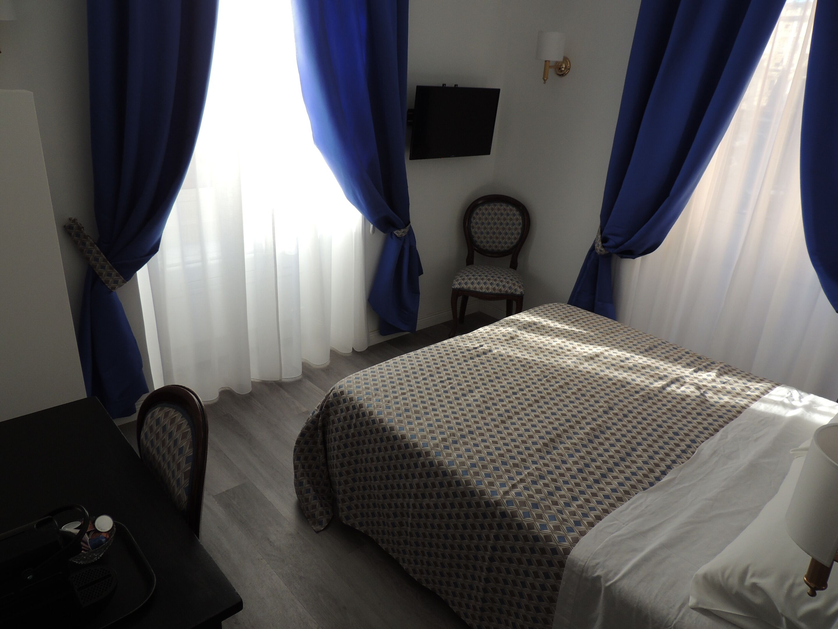 A hotel room with a bed, a chair, a desk, and a TV on the wall.