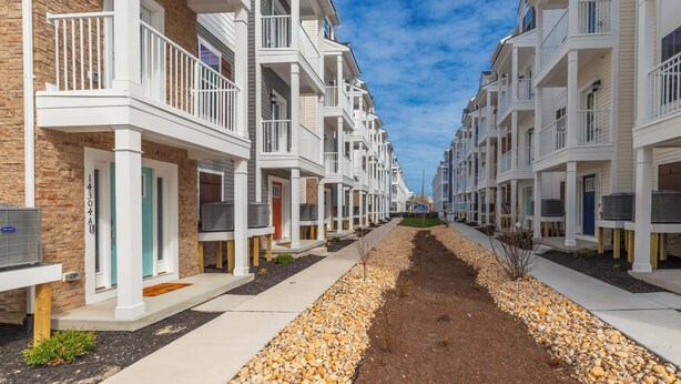 A row of modern apartment buildings with balconies, a central walkway, and a clear sky. - High Tide 3BR Townhome North OC (Ocean City)