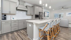 A modern kitchen with grey cabinets, a central island with bar stools, and a large window. - High Tide 3BR Townhome North OC (Ocean City)