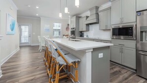 A modern kitchen with a central island, stainless steel appliances, and a dining area with bar stools. - High Tide 3BR Townhome North OC (Ocean City)
