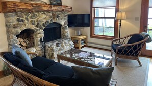 A cozy living room with a stone fireplace, wicker furniture, and a large window.