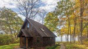 A cabin with a steep roof, a front porch, and a view of a lake surrounded by trees.