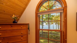 A room with a wooden dresser, a large arched window with a view of trees and a body of water.