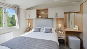 A bedroom with a bed, bedside tables, a dresser, a mirror, and a window with curtains.