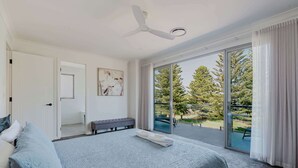 Un dormitorio con cama, una banca, ventilador de techo y puerta corrediza de vidrio que da a un área exterior con árboles.