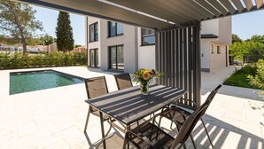 A modern outdoor patio with a pool, a table with chairs, and a pergola overhead. - Luxury apartment Matic Seaview (Funtana)