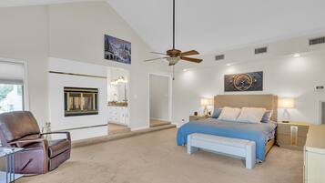 A bedroom with a bed, a chair, a bench, a ceiling fan, and artwork on the walls.