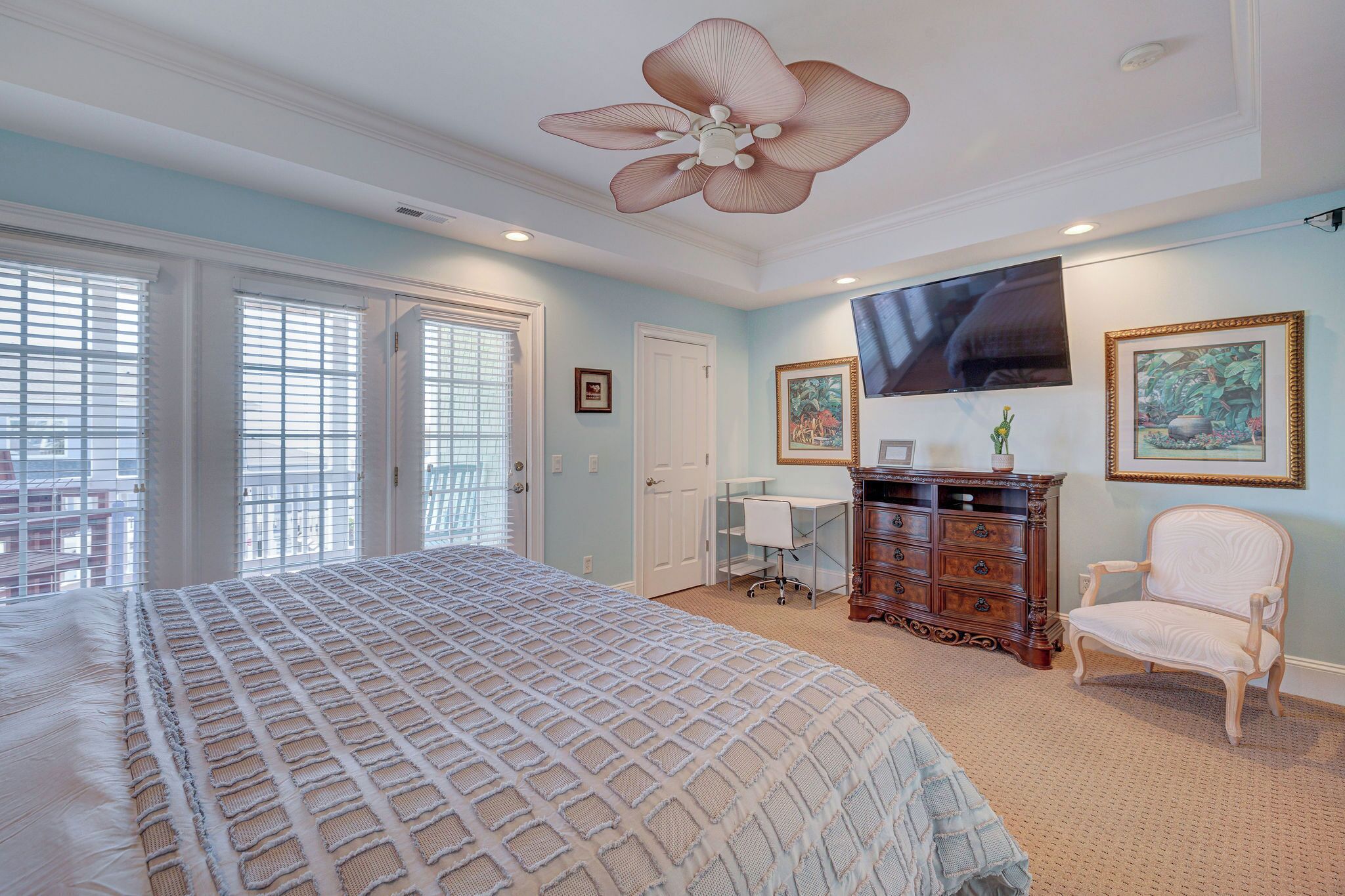 A bedroom with a large bed, a desk, a chair, a dresser, and a ceiling fan.