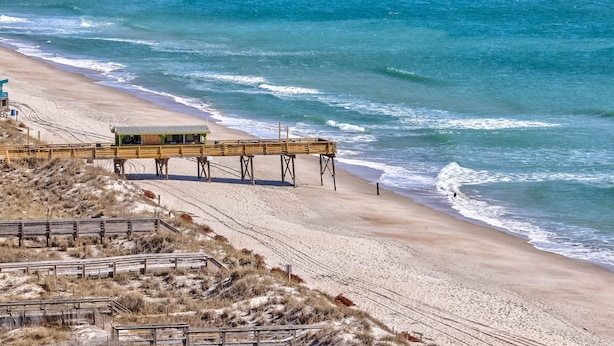 Une plage avec une jetée en bois menant à un poste de surveillance des sauveteurs.
