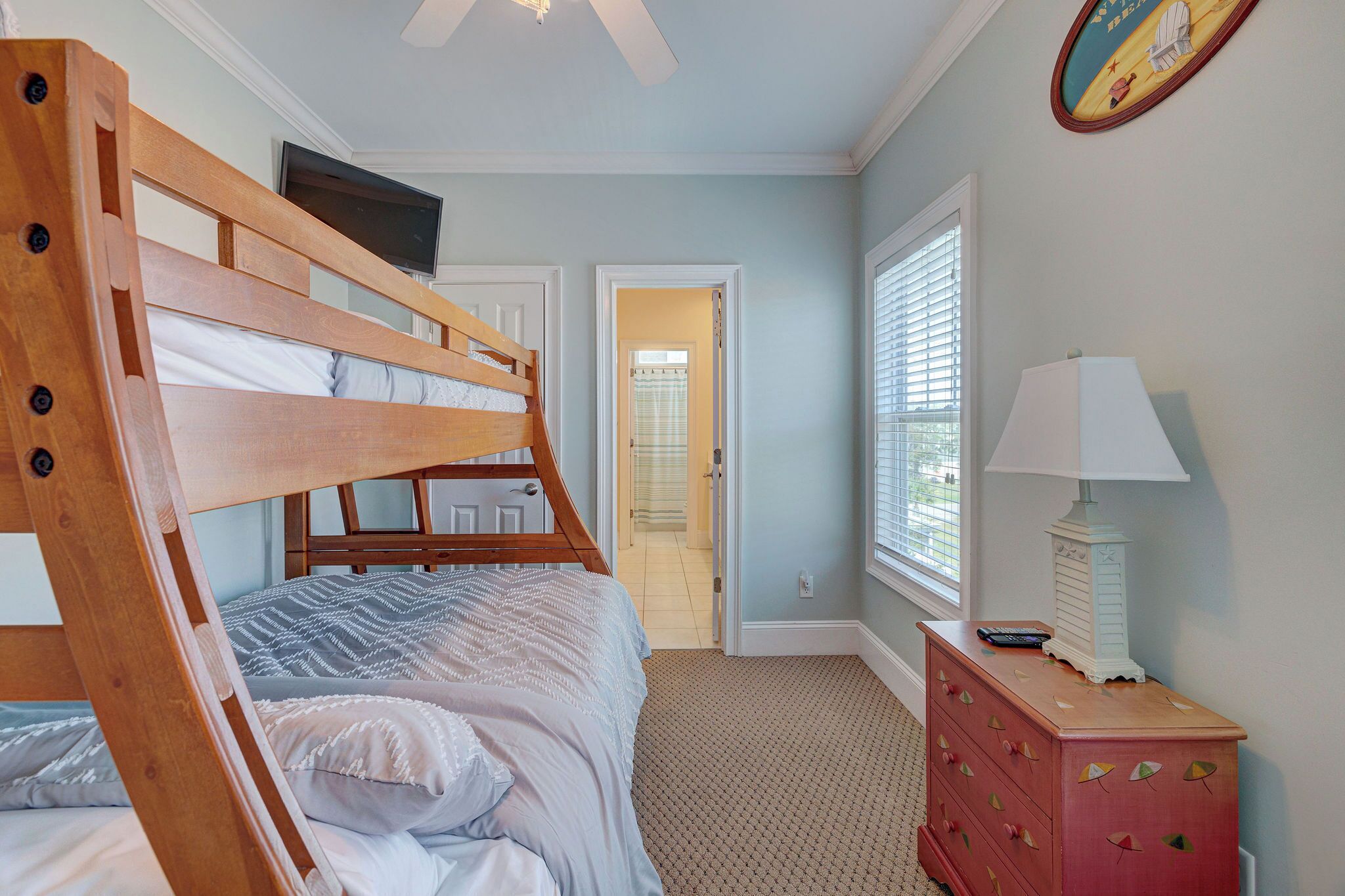 A bedroom with a bunk bed, a dresser, a lamp, and a television.