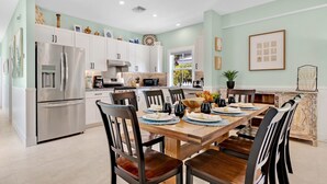 Une cuisine moderne avec des meubles blancs, des appareils en acier inoxydable et un coin repas comprenant une table et des chaises en bois.