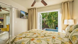 Une chambre à coucher avec un lit, une télévision et une vue sur un jardin, visible par une porte ouverte.