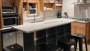 A modern kitchen with a central island, bar stools, built-in ovens, and a stainless steel range hood. - Walk to Downtown Creede | Pet-Friendly | Mountain Views | Fenced Yard (Creede)