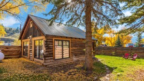 A log cabin with a metal roof, large windows, and a wooden deck. - Walk to Downtown Creede | Pet-Friendly | Mountain Views | Fenced Yard (Creede)